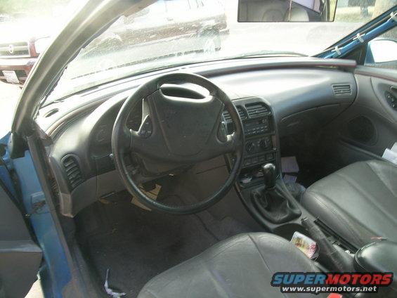 Interior view of a car, showing dashboard, steering wheel, and seats. Another car is visible through the windshield