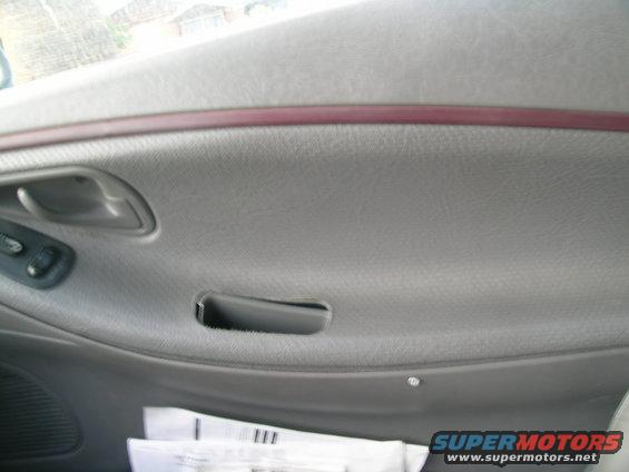 Gray car interior door panel with a red trim strip, door handle, and window controls. Papers are visible in the lower section