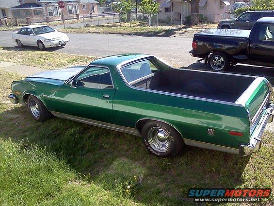 Green pickup truck with a silver hood parked on grass. A white car and a black truck are in the background