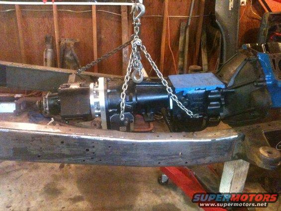 Transmission assembly being lifted by chains and a hoist over a vehicle frame