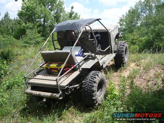 custom off-road buggy with a canopy, cooler, and toolbox in the back, driving on a grassy hill