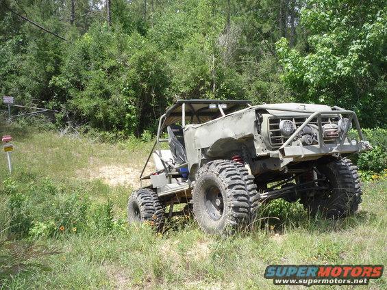 Modified off-road vehicle with large tires and roll cage, parked on grassy terrain