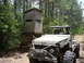 1990 Ford Bronco - This heavily modified off-road vehicle, likely from the 1980s, is parked in a wooded area next to a deer stand.