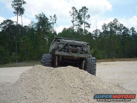 Big tires on a custom military-style truck climbing a pile of gravel