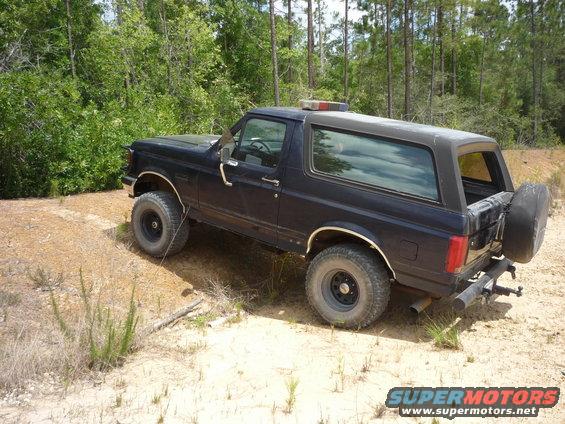 Dark blue SUV with a light bar on the roof, parked on a dirt road with trees in the background