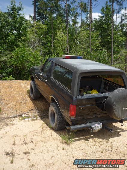 Black 1990 Ford Bronco with light bar on roof, seen from rear-3/4 angle