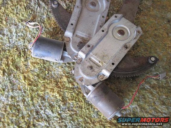 Two power window regulators with motors and wiring, resting on a carpeted surface