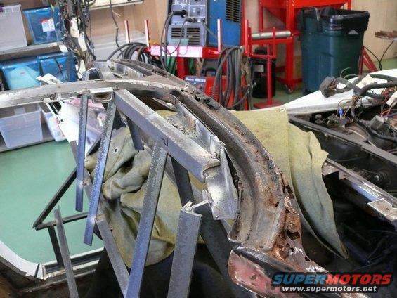 Car frame with rust and metal supports, showing interior wiring and a green trash can in the background
