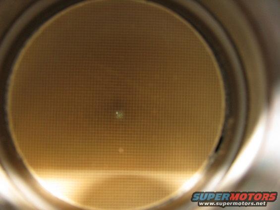 Catalytic converter honeycomb interior, close-up view. Supermotors.net logo visible at bottom right