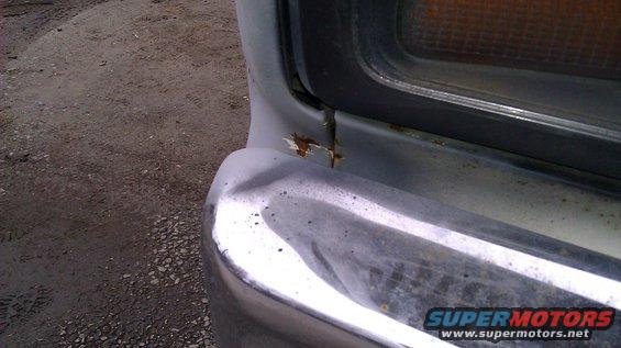 Close-up of a dented chrome bumper and rusted metal on a vehicle's front corner