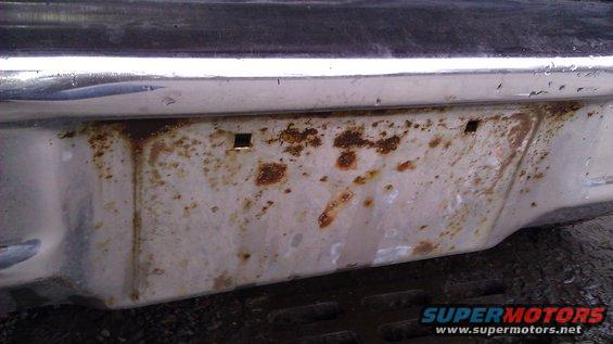 Rusted rear bumper with chrome trim and license plate holes