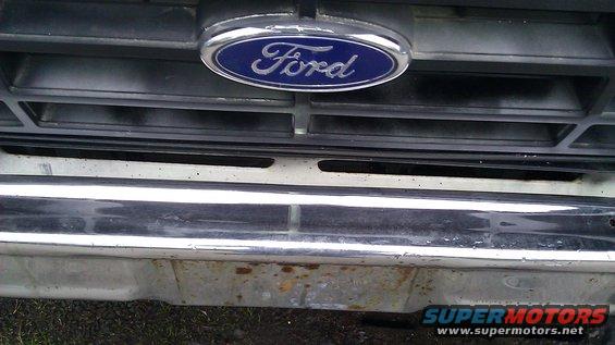 Ford emblem on black grille above chrome bumper with rust spots