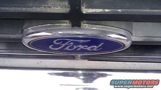 Ford emblem on a chrome grille with black horizontal bars. The emblem is blue with silver script