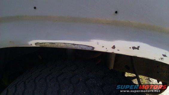 Close-up of rust and chipped paint on a vehicle's fender above the tire