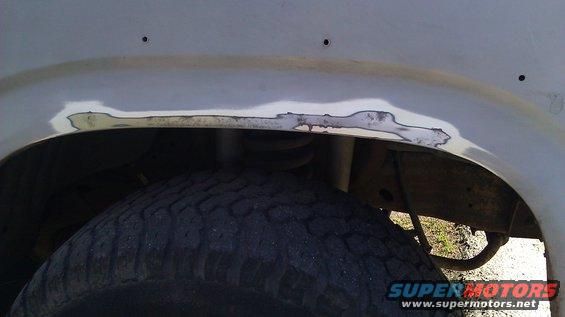 Close-up of body filler on a vehicle's rear wheel well, showing rust repair