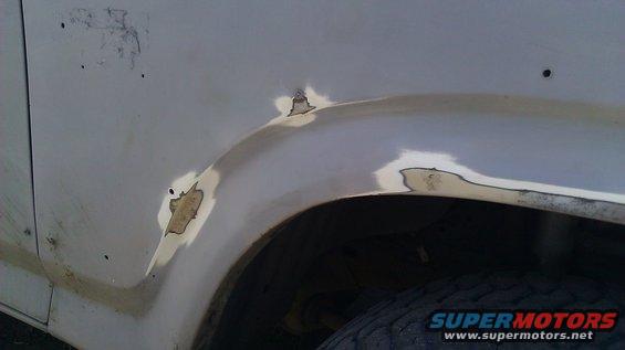 White vehicle fender with rust patches and primer, showing damage around the wheel well