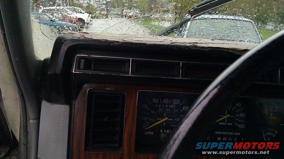 Dashboard of a 1984 Ford Bronco with wood grain trim and a cracked dash pad