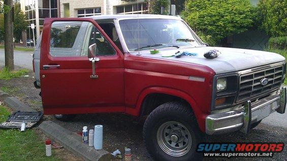 Red and grey SUV with door open, parked on curb with tools and spray cans nearby