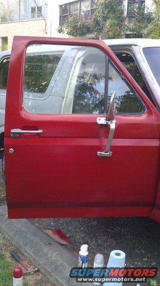 Red truck door with chrome handle and side mirror, next to a white vehicle