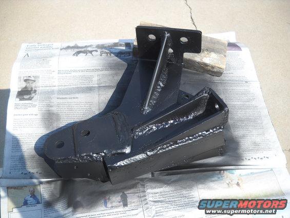 Black metal bracket with welds, resting on newspaper pages