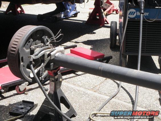 Rear axle assembly with drum brake, supported by jack stands, with welding equipment nearby