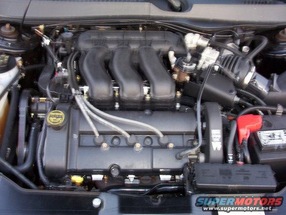 Ford Duratec V6 engine with yellow oil cap and red battery terminal cover. Supermotors.net logo visible
