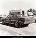1967 Ford Fairlane - A dark 1966 Ford Fairlane race car is parked next to a trailer, displaying sponsor decals and racing slicks.