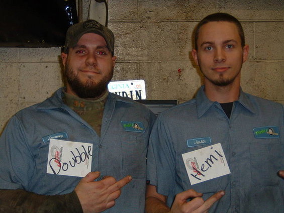 Two men in blue work uniforms, one with a beard and cap, the other clean-shaven, holding name tags that say 'Doubble' and 'Hemi'
