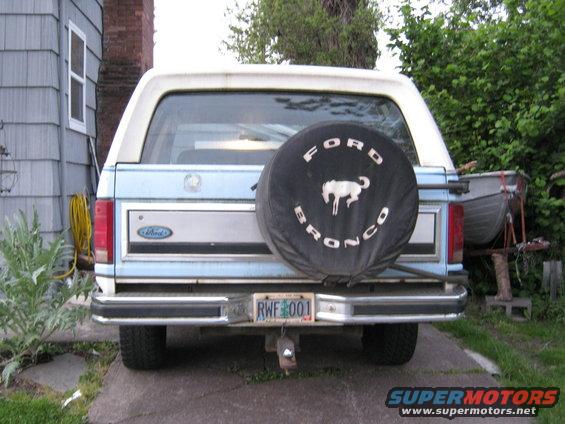 Rear view of a blue and white Ford Bronco with a spare tire cover showing a horse