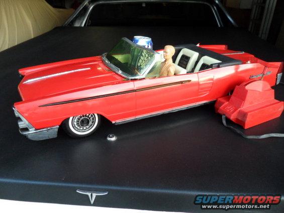 Red toy convertible with a doll driver and a blue light on the windshield