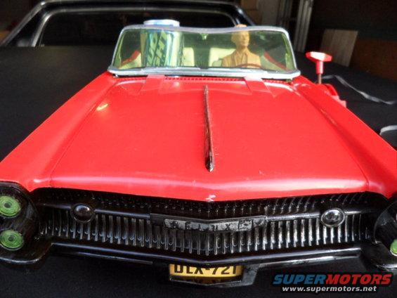 red toy car with a mannequin driver, parked behind a black vehicle
