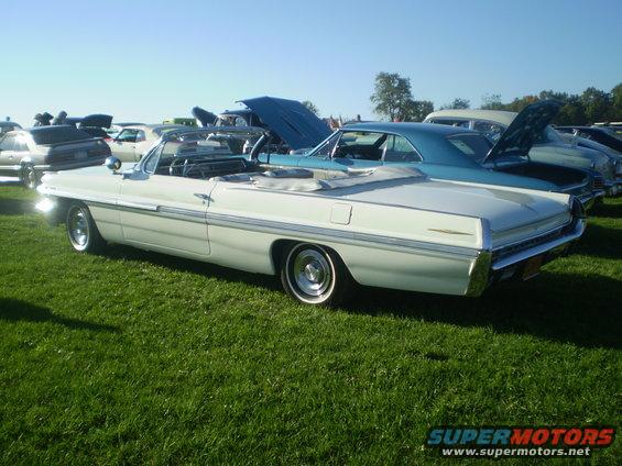White convertible with chrome trim, parked on grass at a car show