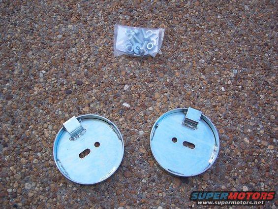 two round metal air suspension parts and a bag of bolts on a gravel surface