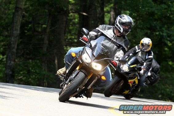 Two motorcycles on a winding road, one in the foreground with its headlights on