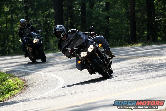 Two motorcycles riding on a paved road through a wooded area