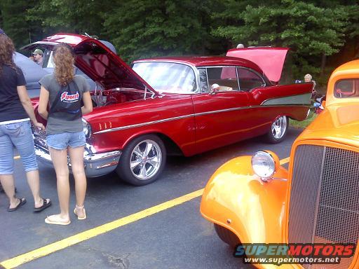 Red 1957 Chevrolet Bel Air coupe with hood open, parked next to an orange hot rod