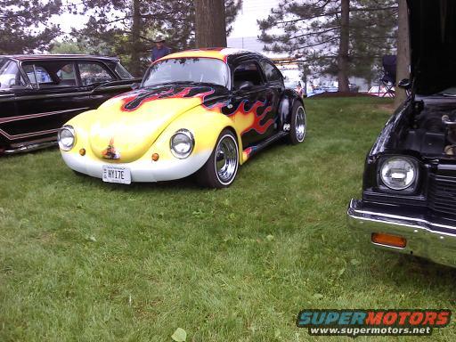 Yellow Volkswagen Beetle with flame graphics and custom wheels parked on grass next to a black car