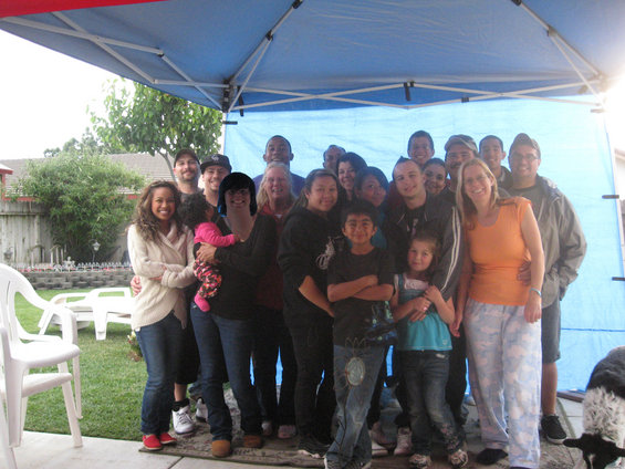 group of people, including adults and children, posing for a photo under a blue tent in a backyard