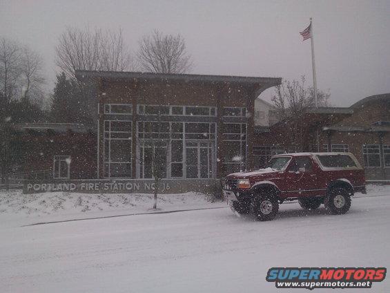 Red SUV driving past Portland Fire Station No. 16 in the snow