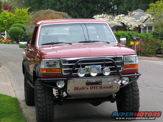 Red Ford Bronco with a brush guard and winch, parked on a residential street