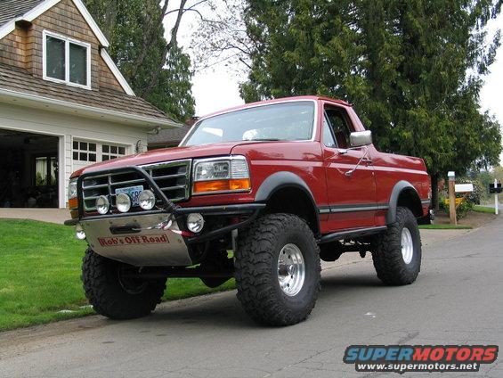 Red 1989 Ford Bronco with off-road bumper and large tires parked in driveway