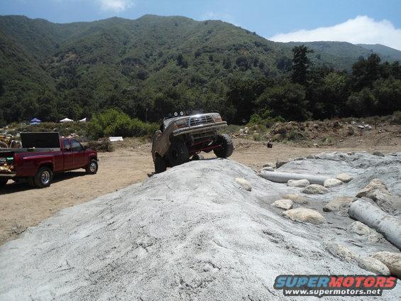 Off-road truck climbing a dirt mound with a red pickup truck in the background