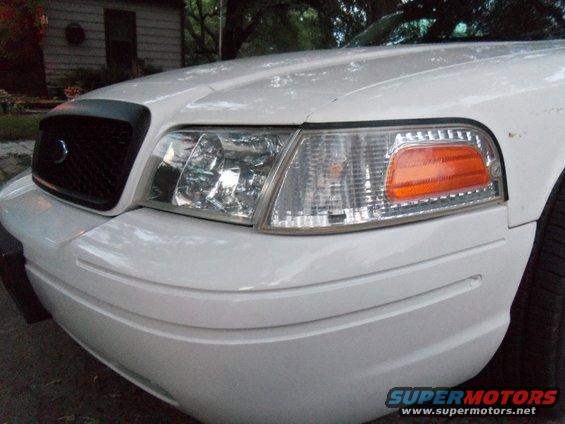 Front corner of a white sedan, showing the headlight, grille, and bumper