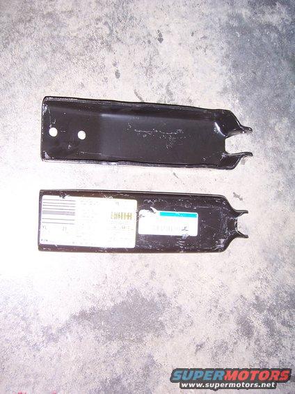 Two black metal brackets with labels on one, resting on a concrete surface