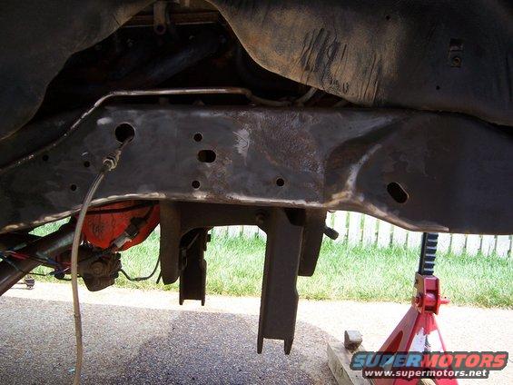 Underside of a vehicle showing the frame, suspension parts, and a red jack stand