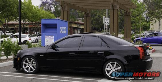 Black Cadillac sedan parked, side view, with aftermarket wheels