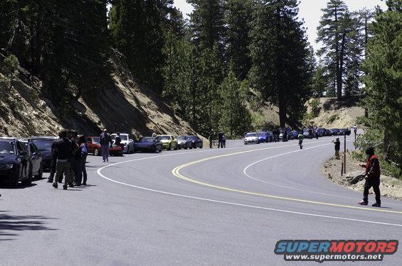 Cars parked on a winding mountain road with trees and a slope