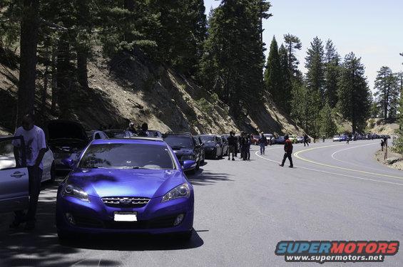 Blue Hyundai Genesis coupe parked on a mountain road with other cars and people