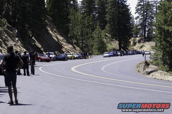 Cars parked along a winding mountain road with people standing around