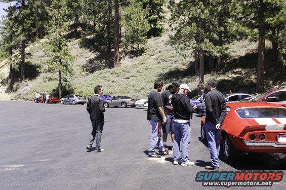 Red muscle car with white stripes, rear view. People gathered around